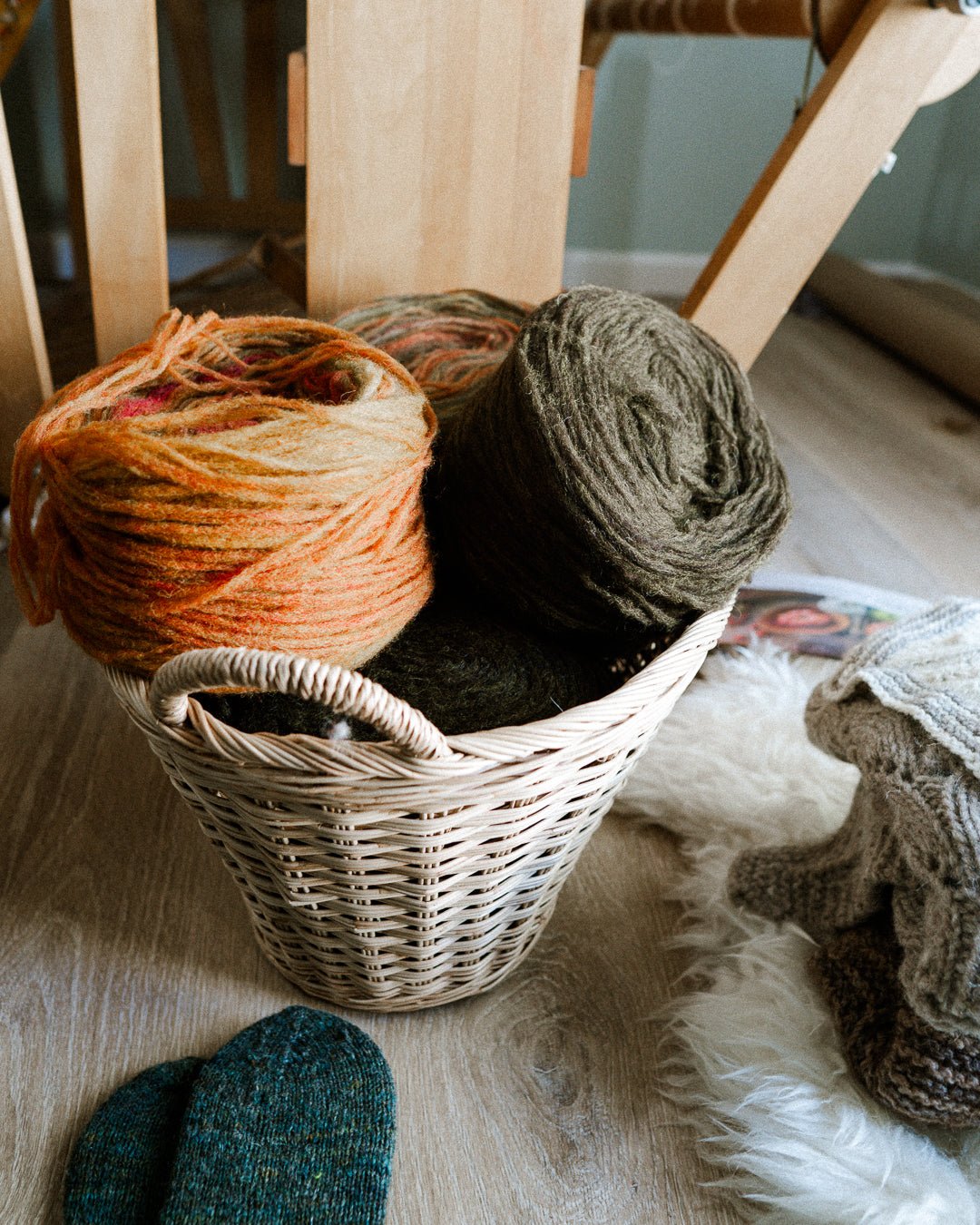 a basket set on the floor with various colors of unspun yarn in it, in oranges and browns