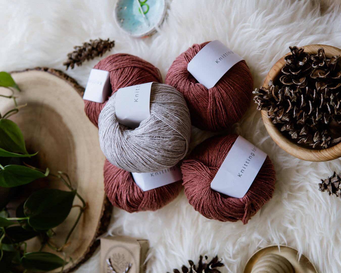 Four balls of red yarn below one ball of beige yarn on a holiday flat lay with pinecones and trinkets.